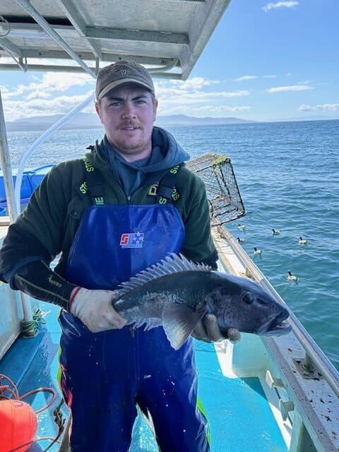 A man in an apron holding a fish on a boat.
