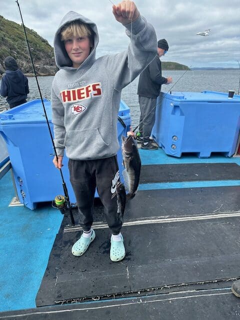 A boy holding up a fish on a boat.
